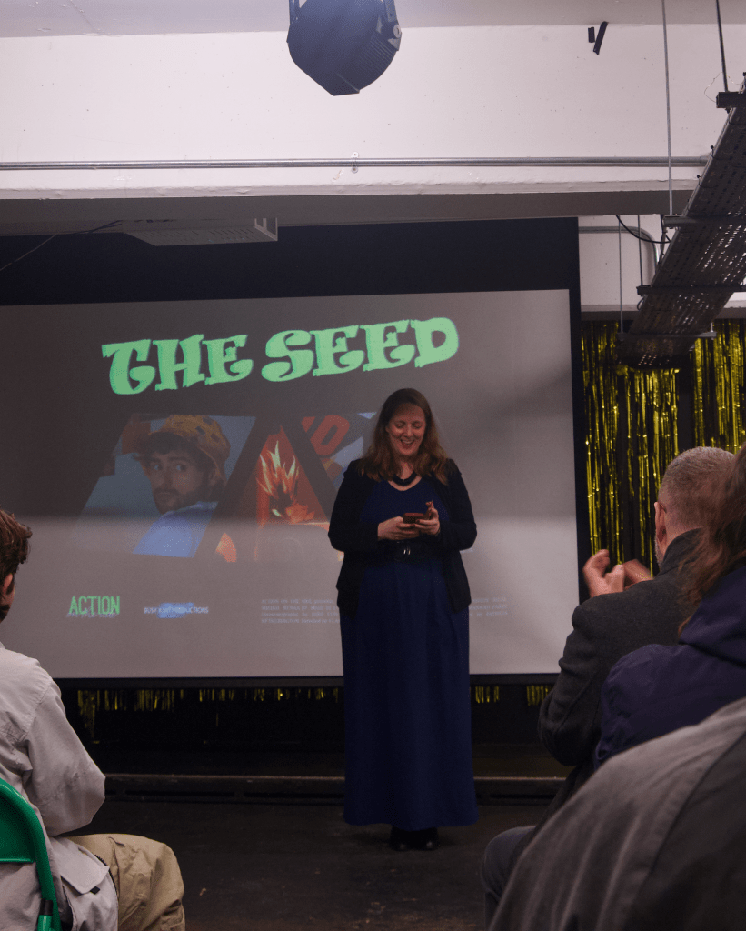 Patricia stands in front of a screen with the promotional image for The Seed film.